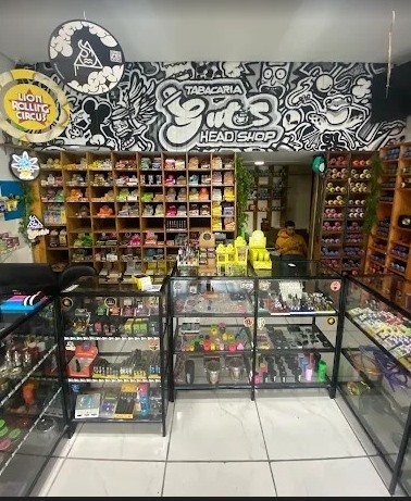 Interior da Tabacaria Guto's Head Shop, com mural grafitado, prateleiras de madeira e vitrines